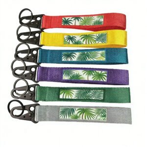 Bespoke Woven Ribbon Keychains Tropical Palm Motif Charms A flat-lay array of six vibrantly hued woven keychains, each emblazoned with verdant tropical palm prints atop a central white cartouche and crowned with matte black triangular lobster clasps, showcased against a pristine white void.