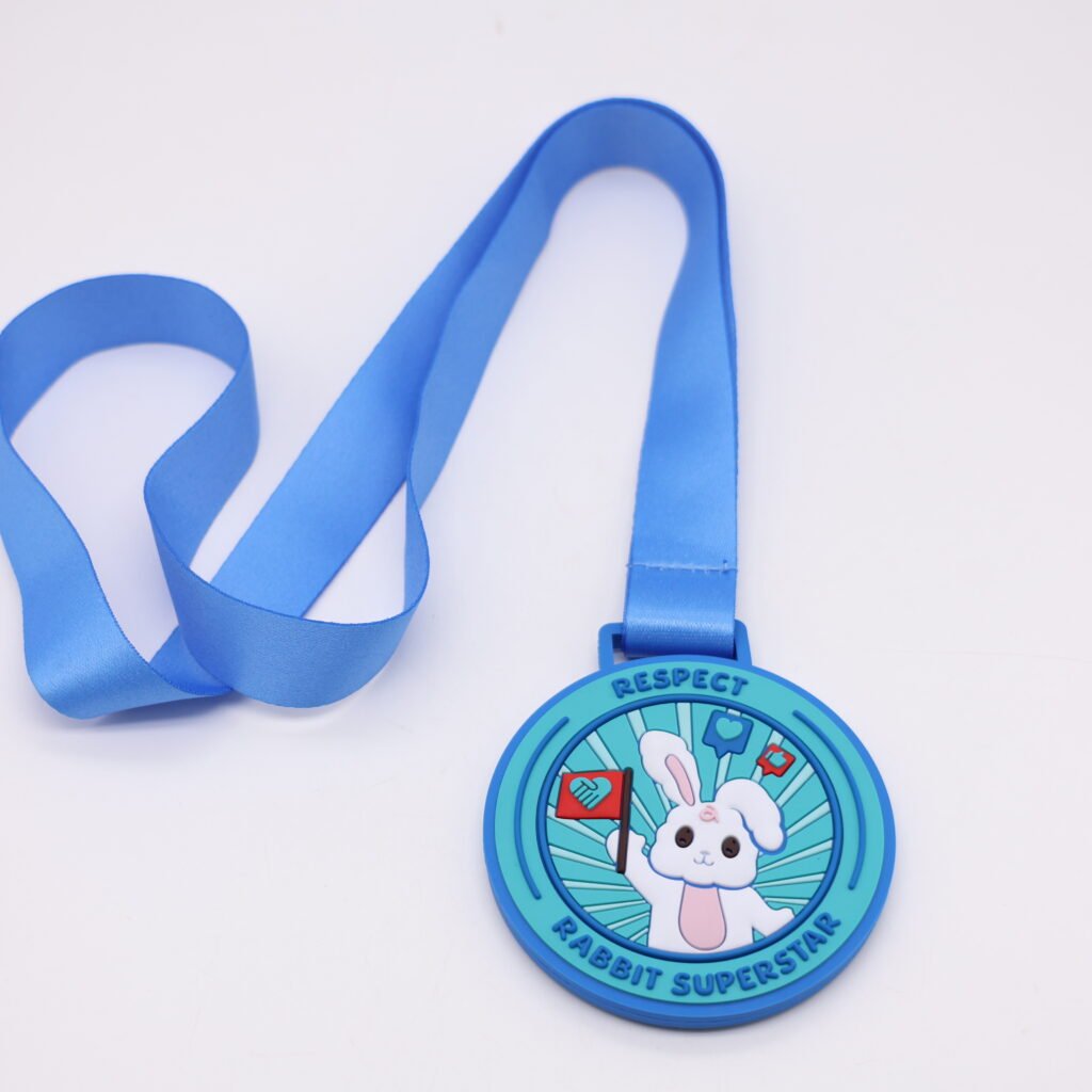 A vibrant custom PVC medals featuring a blue gradient circle. The center shows a cute white cartoon rabbit holding a red flag, surrounded by like/comment icons and radial lines. Text reads "RESPECT" at the top and "RABBIT SUPERSTAR" at the bottom. It hangs from a wide blue polyester neck ribbon.