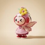 A cute 3D PVC soft rubber keychain in the shape of a cartoon fairy girl with pink layered dress, yellow flower hair accessory, translucent wings, and a playful winking expression.