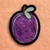 Custom chenille patch featuring purple cartoon fruits with smiley faces, green leaves, and brown stems, finished with black overlock edging, on a light orange linen background