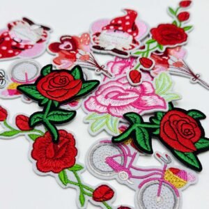 Custom embroidered fabric patches featuring red roses, pink large flowers, a vintage bicycle, a heart girl, and other designs, available with sew-on, Velcro backing, or iron-on backing — scattered on a pure white background with fine, full stitching