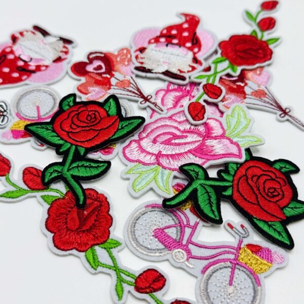 Custom Embroidered Fabric Patch Custom embroidered fabric patches featuring red roses, pink large flowers, a vintage bicycle, a heart girl, and other designs, available with sew-on, Velcro backing, or iron-on backing — scattered on a pure white background with fine, full stitching