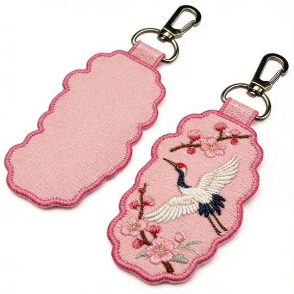 Custom Embroidered Keychain Chinese Style Crane & Cherry Blossom Auspicious Cloud Charm Pink auspicious cloud-shaped embroidered keychain featuring an embroidered red-crowned crane in flight with blooming pink cherry blossom branches on the front, in fresh, understated colors, with a metal lobster clasp, displayed front and back on a pure white background