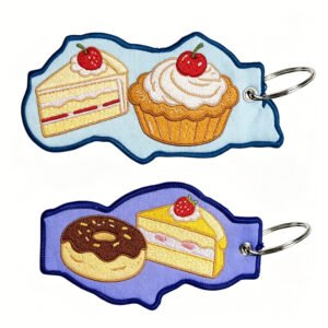Pair of custom embroidered keychains with cake slice, cupcake, donut & strawberry designs on blue & purple backgrounds