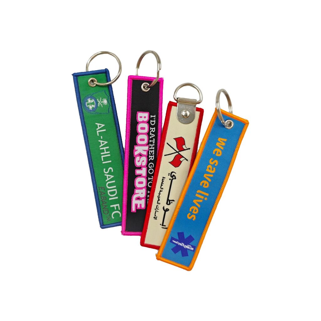 Set of four colorful embroidered keychains on woven tape; features a football club crest, "I'd Rather Go To Bookstore" text, and a medical star of life symbol; attached to silver D-rings.