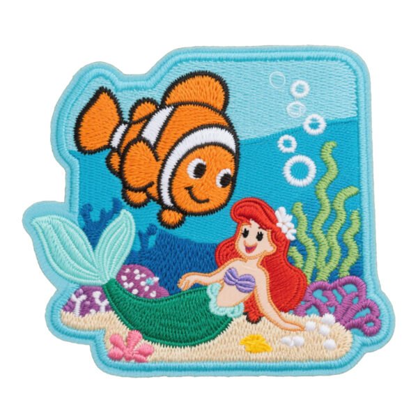 Custom embroidered patch featuring a Little Mermaid Ariel and clownfish Nemo underwater scene with seaweed, bubbles, coral, and sandy seabed, finished with a light blue overlock border, on a pure white background