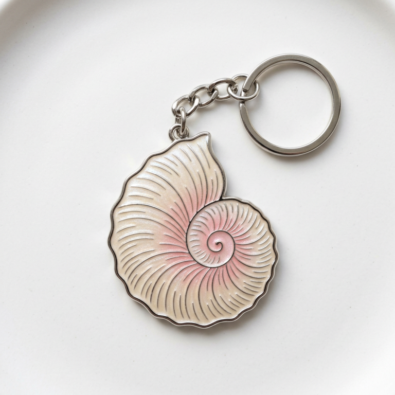 Elegant nautilus shell metal keychain with soft pink-to-purple gradient enamel infill; silver-toned zinc alloy body with a spiral texture, attached to a keyring via a short chain.