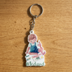 Custom printed PVC keychain featuring a cute cartoon boy painting with palette and paper, 'Médard' text on wood background