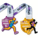 Two vibrant purple and yellow kids' sports-themed PVC rubber medals featuring running figure silhouettes and "DL Kids Football Award" text, paired with white polyester ribbons printed with brand logos, isolated on plain white background.
