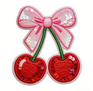 Custom sequin embroidered patch featuring a pink sequin bow paired with two red sequin cherries with green stems and white overlock edging, on a pure white background