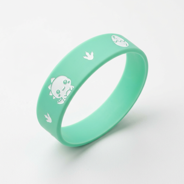 Custom Silicone Wristband Cartoon Dinosaur Debossed Printed Bracelet Mint green silicone wristband featuring cute cartoon dinosaur, dinosaur footprint, and bird-shaped white debossed prints on the surface, displayed on a pure white background