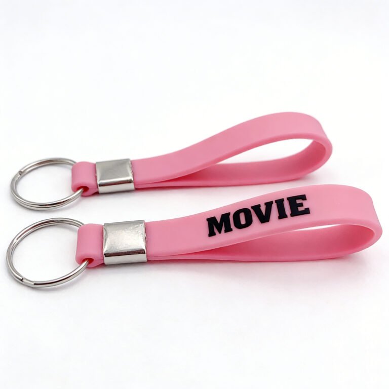 Custom pink silicone wristband keychain with black "MOVIE" lettering printed on the surface, featuring a metal connector and keyring — doubling as a wrist strap and keychain charm