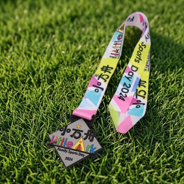 Custom soft PVC family sports day medal with a triangular contour-cut body featuring "小方舟 Little Ark Family Sports Day 2024" lettering and colorful tent artwork, paired with a colorful geometric patterned strap (with "小方舟" and "Sports Day 2024" text), placed on green lawn