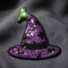 Custom sequin embroidered Velcro patch featuring a Halloween witch hat design with a purple-to-black gradient sequin finish and shimmering green tip, fully backed with Velcro, displayed against a dark gray fabric background