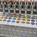An automated multi-needle dispensing machine precisely injecting vibrant liquid PVC colors into custom keychain molds on a factory production line.