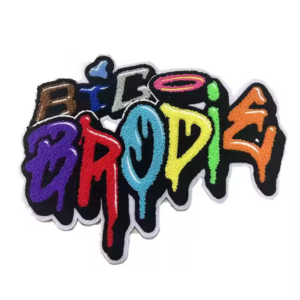 A street art style custom chenille patch. The text "BIG BRODIE" is rendered in a bubble graffiti font with a rainbow gradient (brown, blue, pink, purple, red, cyan, yellow, green, orange). It features a thick, plush chenille texture, a black outline, and a clean white merrowed edge.