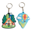 Set of 3D PVC soft rubber keychains featuring a fairytale forest cottage with green trees, red-and-white spotted mushrooms and a wooden house, plus a red-and-yellow striped hot air balloon against a blue sky with clouds; vibrant colors with a silver metal split ring for daily key organization or bag decoration.