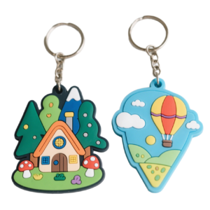 Set of 3D PVC soft rubber keychains featuring a fairytale forest cottage with green trees, red-and-white spotted mushrooms and a wooden house, plus a red-and-yellow striped hot air balloon against a blue sky with clouds; vibrant colors with a silver metal split ring for daily key organization or bag decoration.