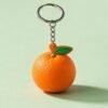 A lifelike 3D orange-shaped PVC soft rubber keychain featuring a vibrant orange peel texture, green stem and leaf detail; attached via a short metal chain to a standard silver split ring, offering a playful and tactile accessory.