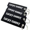 Set of 4 identical black rectangular embroidered keychains featuring bold white Old English font "LUCKY GHOST" text with fine merrowed edges; finished with a silver metal split ring, embodying dark streetwear and punk aesthetics for everyday carry decor.
