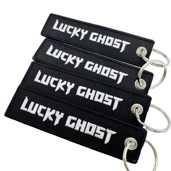 Set of 4 identical black rectangular embroidered keychains featuring bold white Old English font "LUCKY GHOST" text with fine merrowed edges; finished with a silver metal split ring, embodying dark streetwear and punk aesthetics for everyday carry decor.